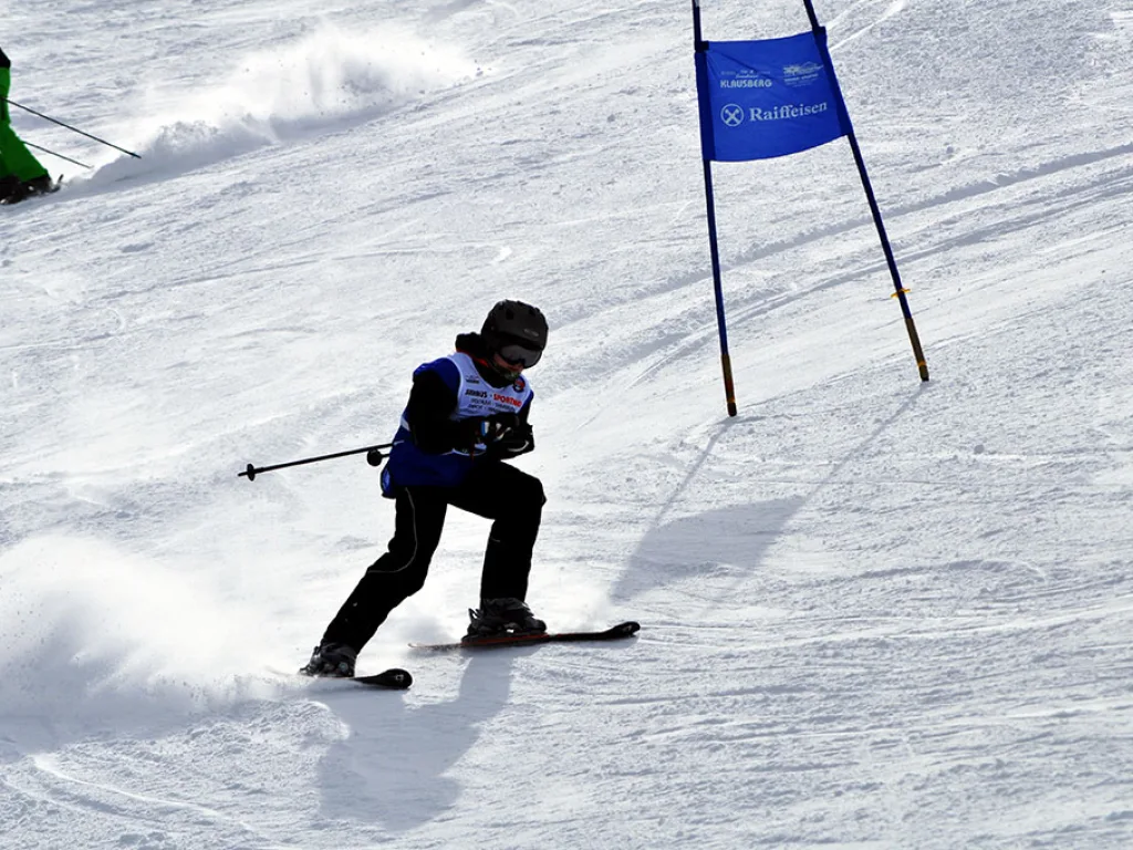 Snowboarder mit aufstiebendem Schnee neben dem blauen Tor.